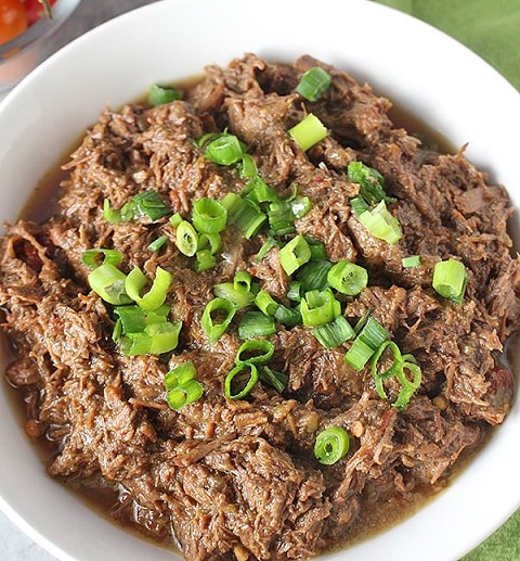 Beef Barbacoa in a white bowl with sprinkled spring onion on top